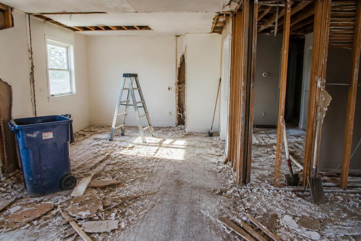 Residential demolition scene with a blue bin, ladder, and debris in a room