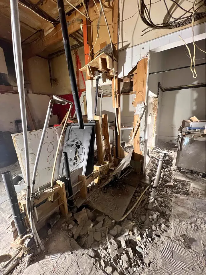 Commercial unit wall torn down to framing with wiring hanging and debris on the floor