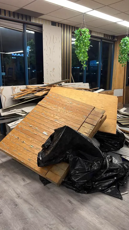 Office showroom with wood wall panelling pulled down and bagged debris on the floor