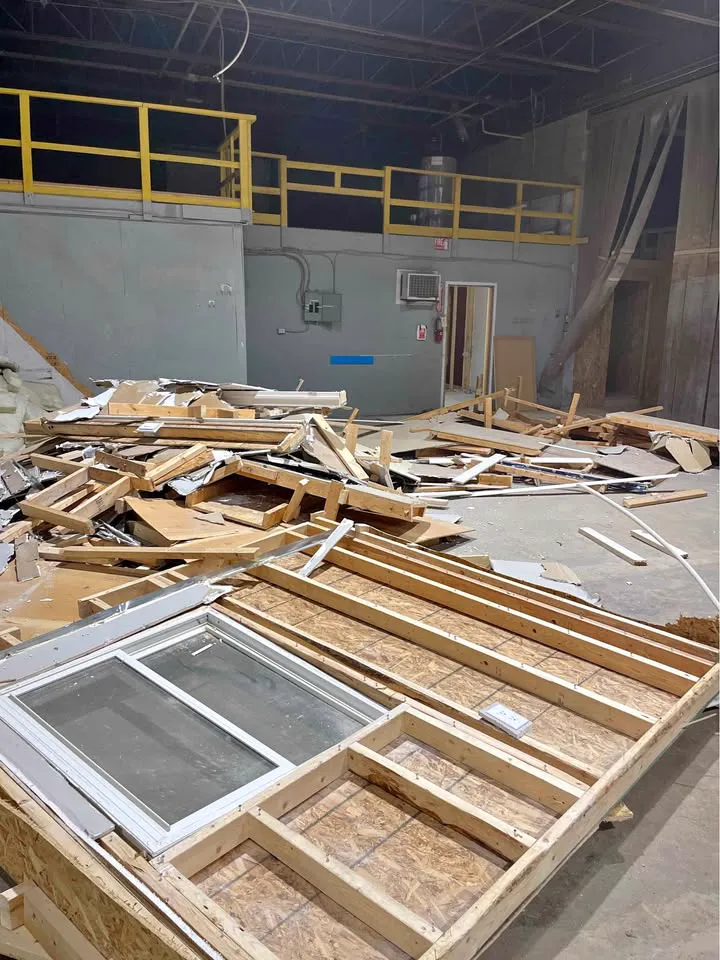 Warehouse floor covered with torn-down wood-framed walls below a yellow mezzanine rail