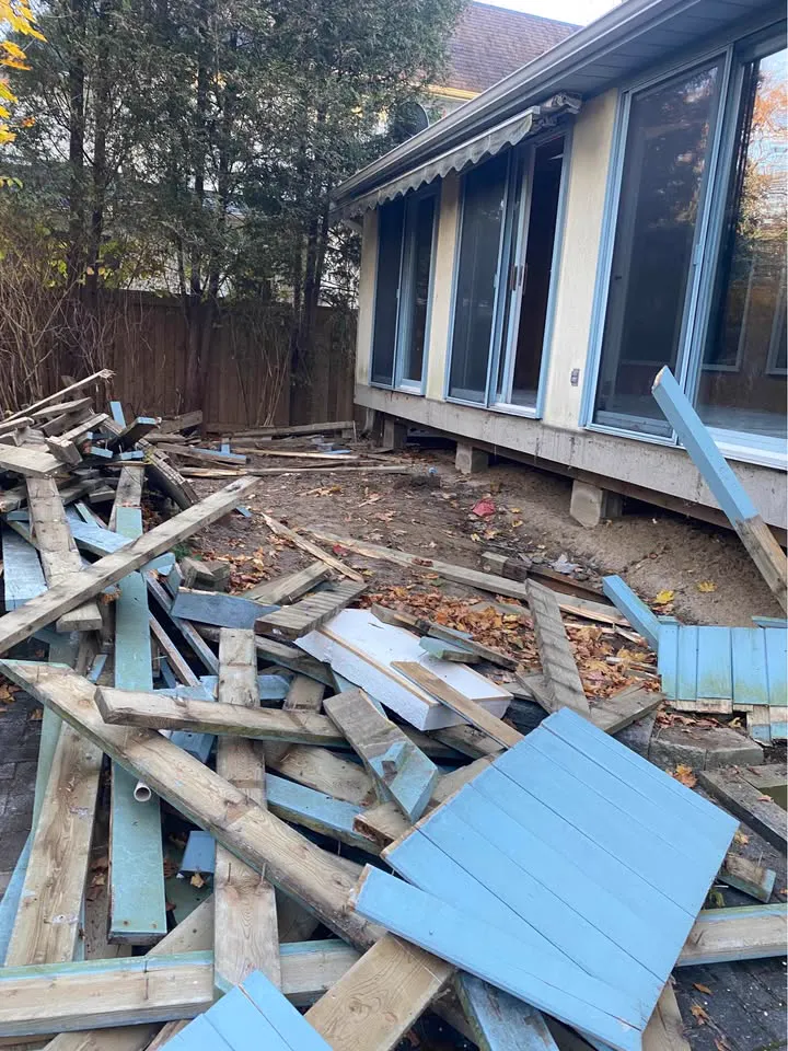 Wood deck torn apart beside a sunroom with boards and decking piled in the yard