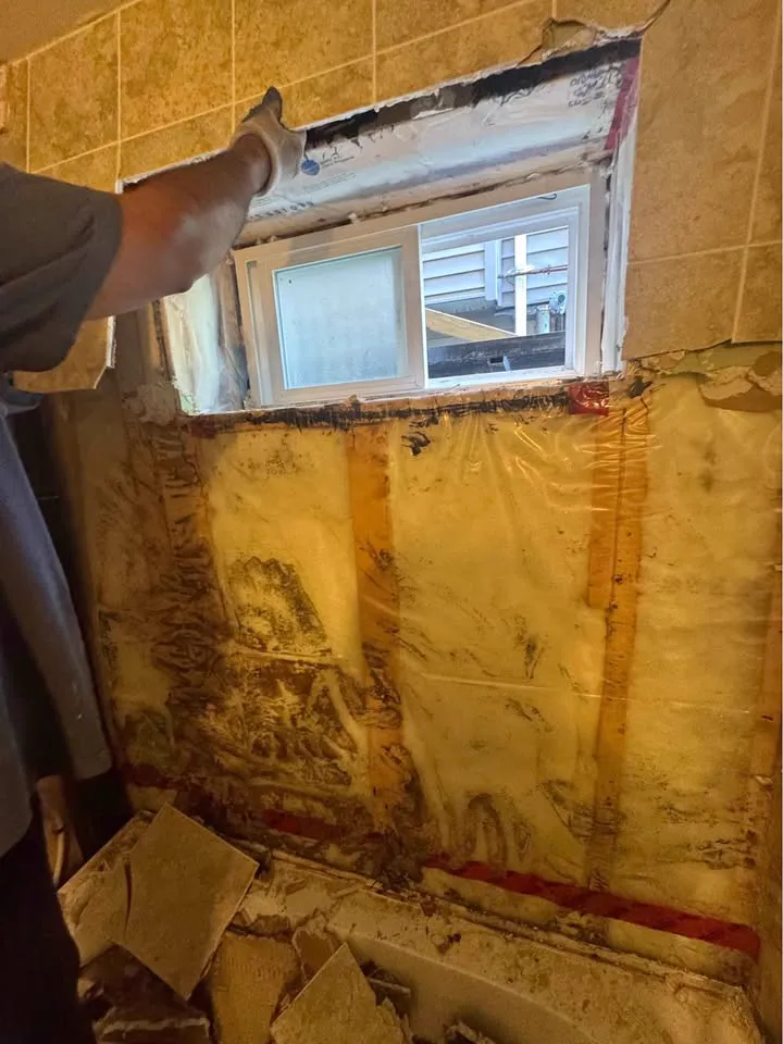 Basement shower corner opened to framing and vapour barrier below a window