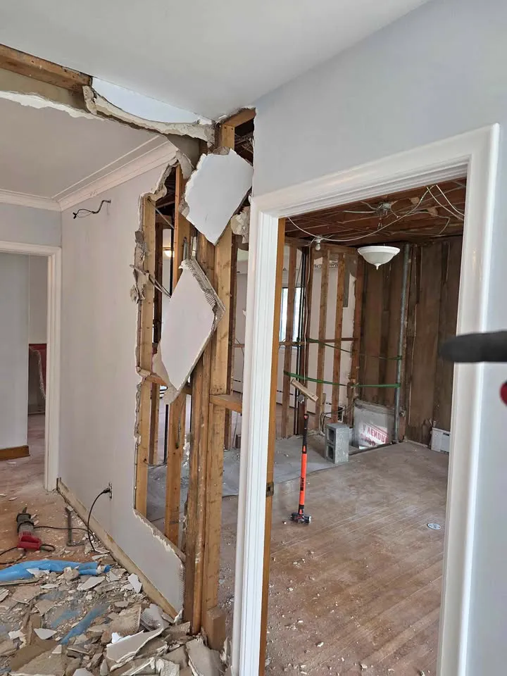 Doorway opened through a wall with studs exposed into a gutted bathroom