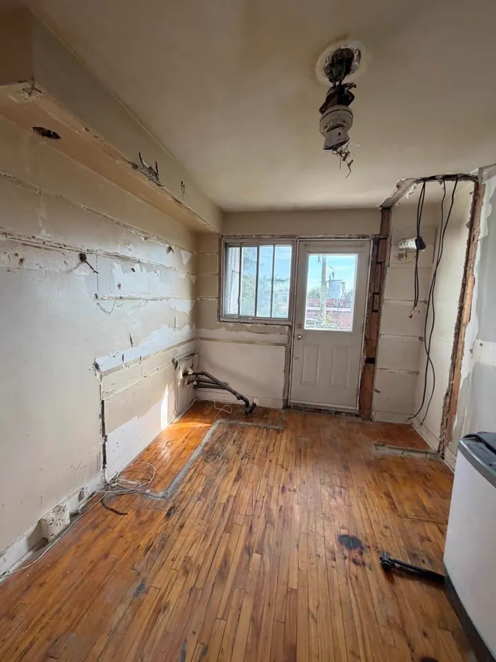 Room with the drywall stripped to lath and the hardwood floor left in place