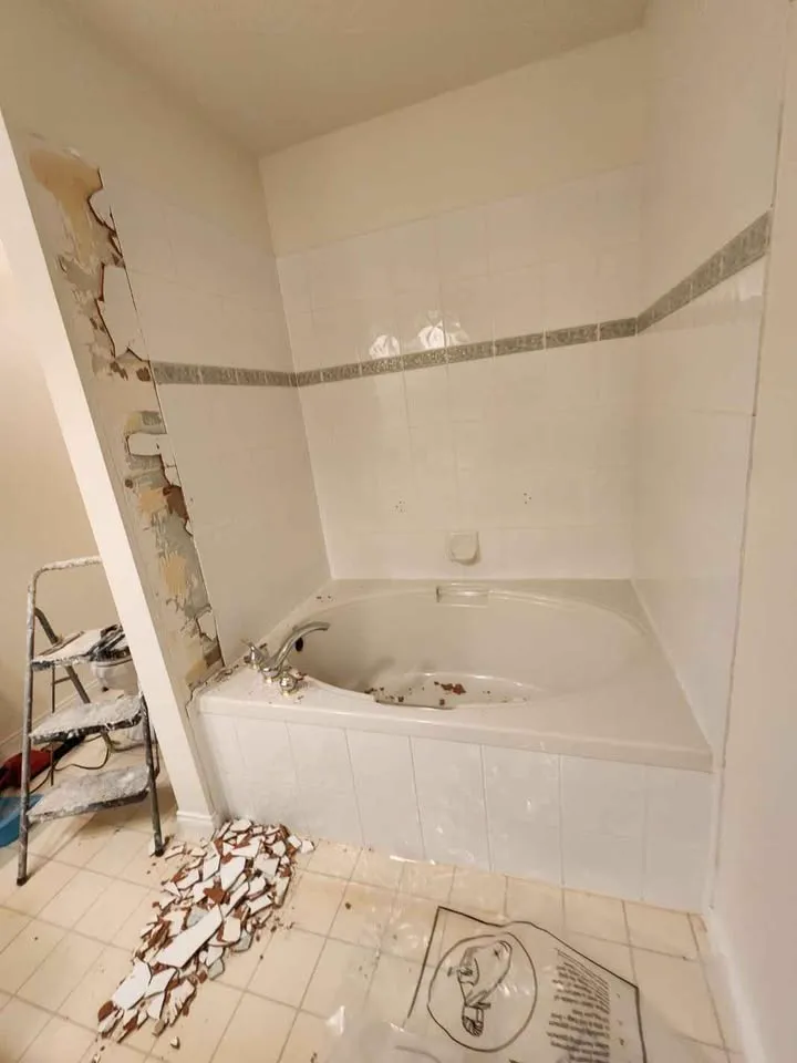 Bathroom with tub surround tiles partly removed and tile debris on the floor
