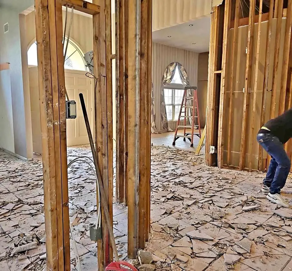 Crew member clearing plaster from a room opened up to the studs