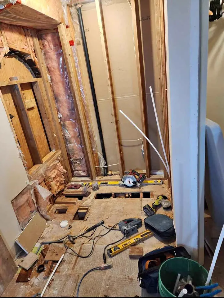 Bathroom floor cut open with tools and levels laid out on the subfloor