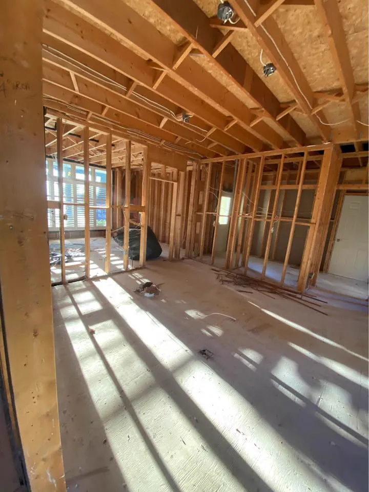 Large room gutted to wall studs and ceiling joists with sunlight across the subfloor
