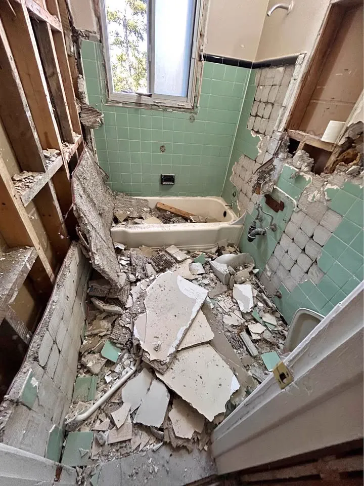 Green-tiled bathroom with the tiles and tub surround torn out