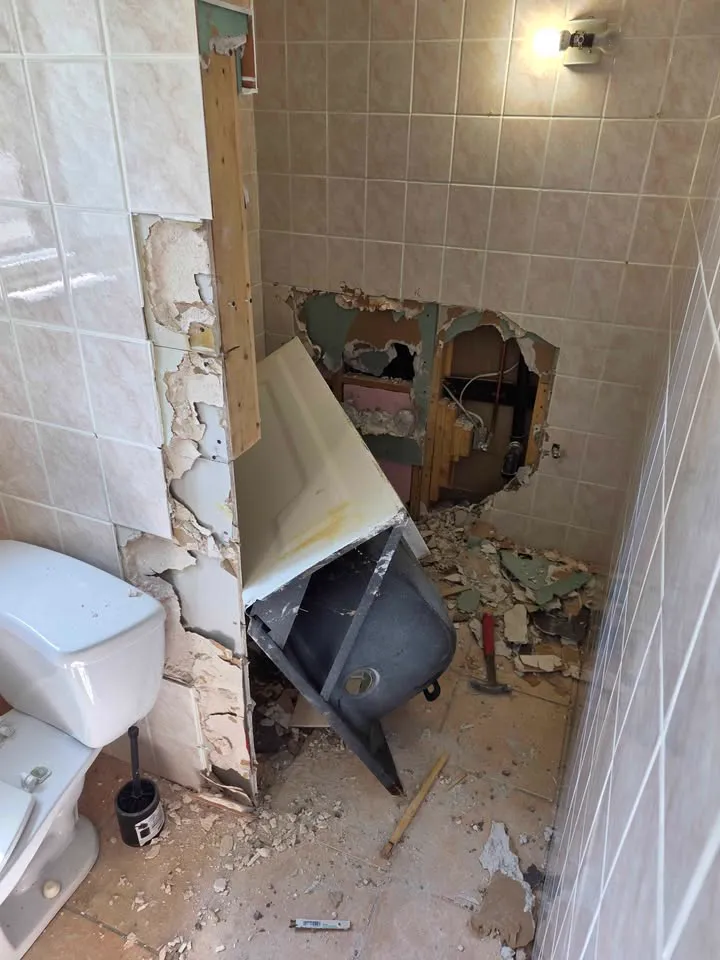 Bathroom wall tiles removed around a tub with a hole opened in the wall