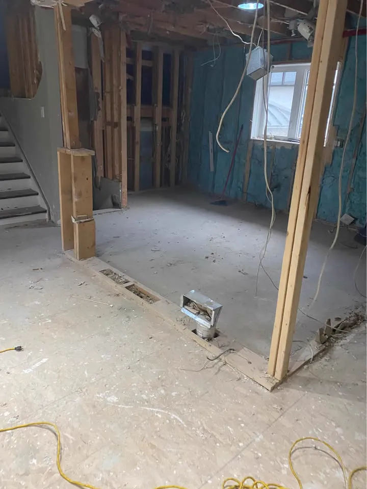 Room gutted to studs with blue insulation and the stairs to one side