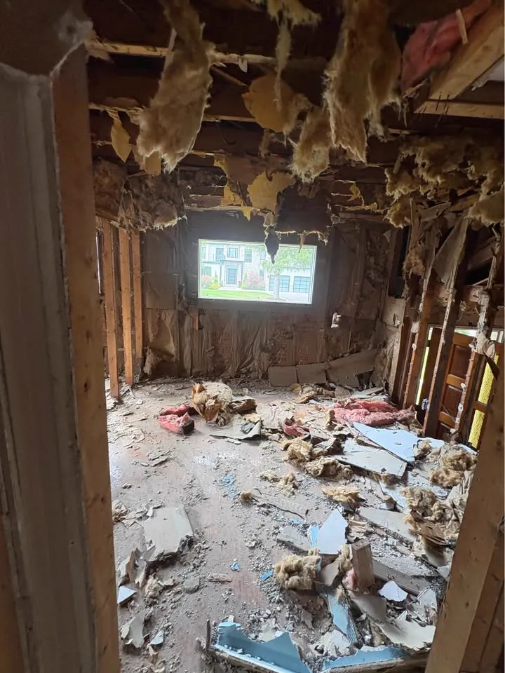 Room with insulation hanging from an open ceiling and debris on the floor