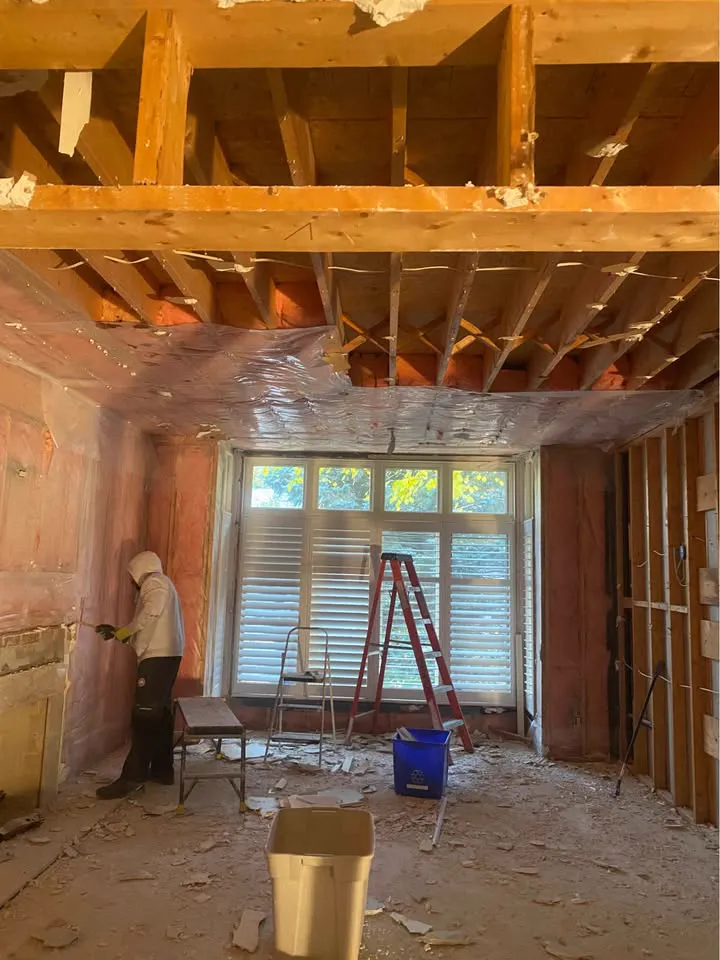 Crew member working in a living room stripped to the ceiling joists
