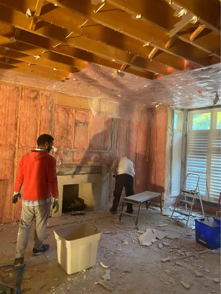 Two crew members stripping walls beside a fireplace