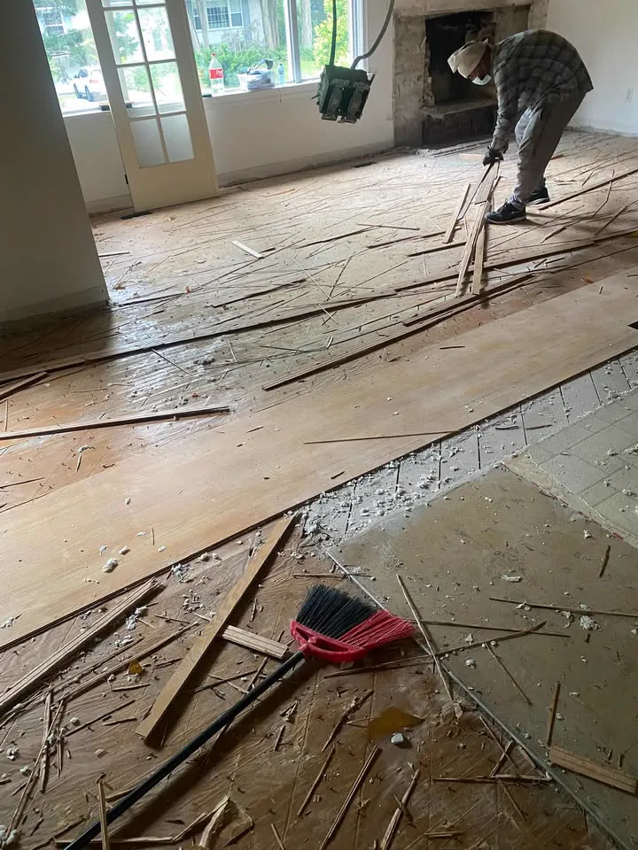 Crew member pulling up hardwood flooring across a room