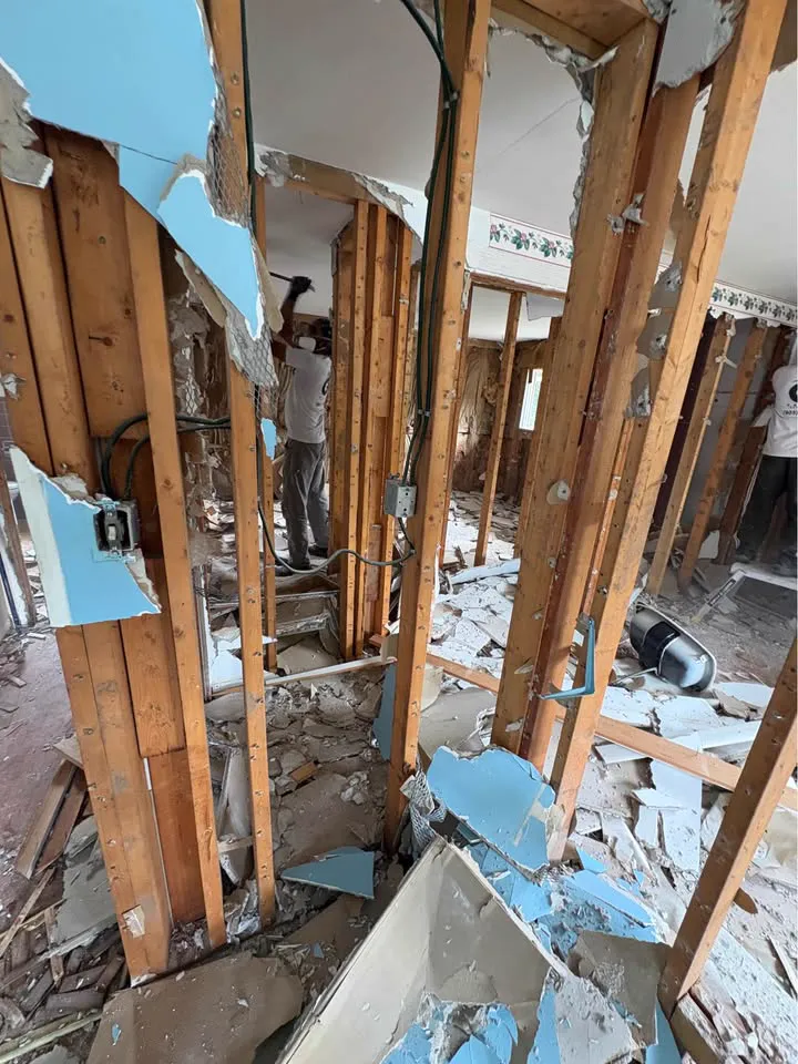Crew stripping plaster walls to the studs with blue board debris below