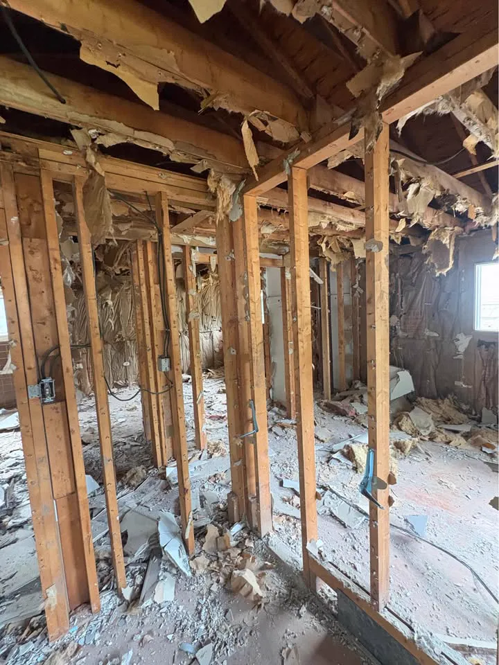 Wall framing exposed after plaster removal with debris along the base