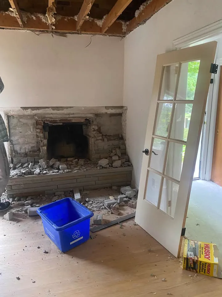 Fireplace surround and floor cleared in a stripped room with a recycling bin