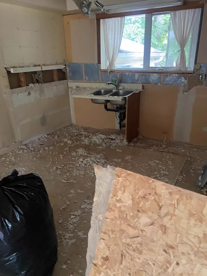 Kitchen with cabinets and counters removed and the sink plumbing exposed