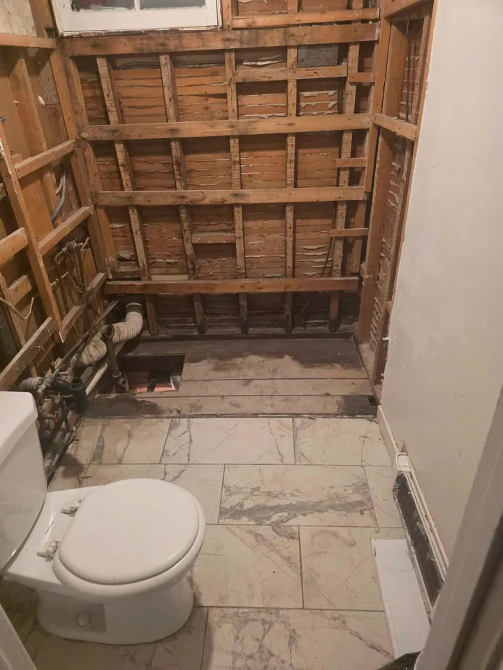 Small bathroom stripped to lath with the toilet and tile floor still in place