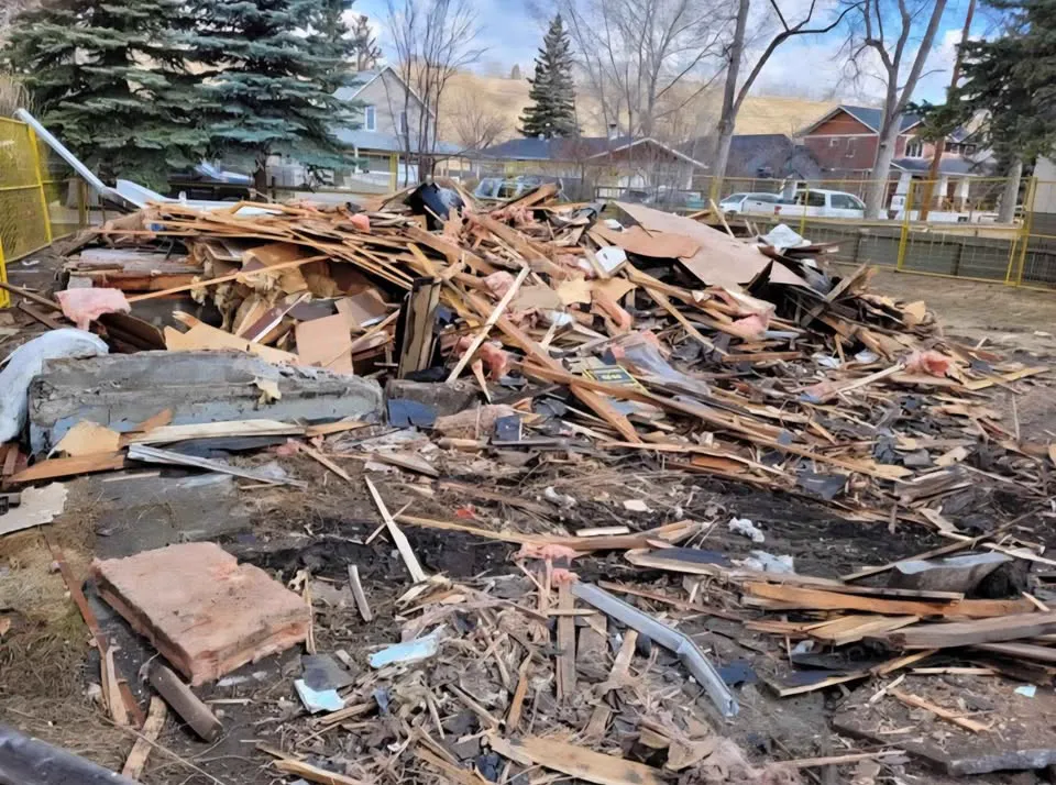 Large pile of wood debris on a fenced lot after a house was taken down
