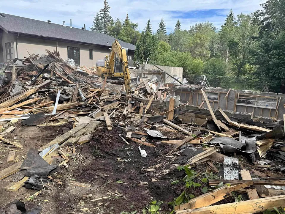 Excavator sorting house demolition debris with the foundation walls still standing