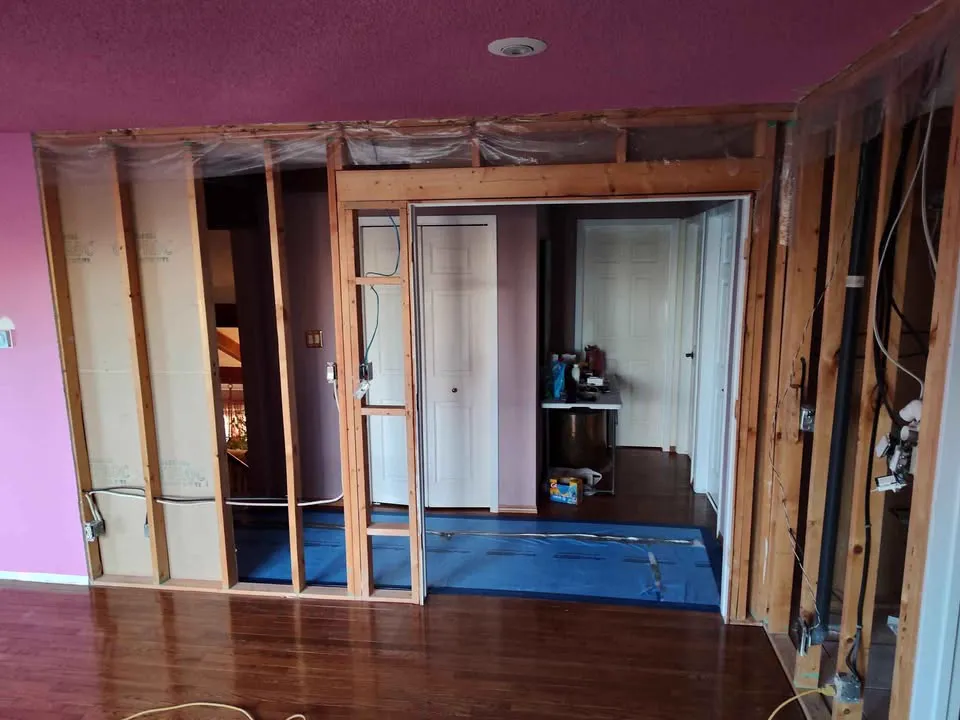 Wall removed to the framing between two rooms with blue floor protection laid down